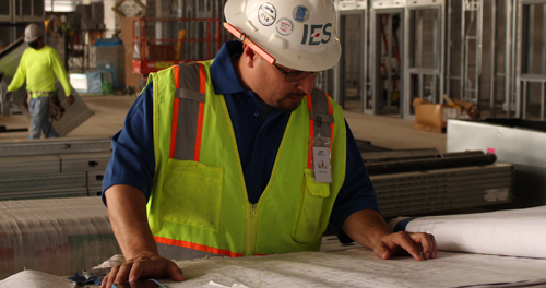 a supervisor in an IES hard hat inspecting blueprints on a construction site
